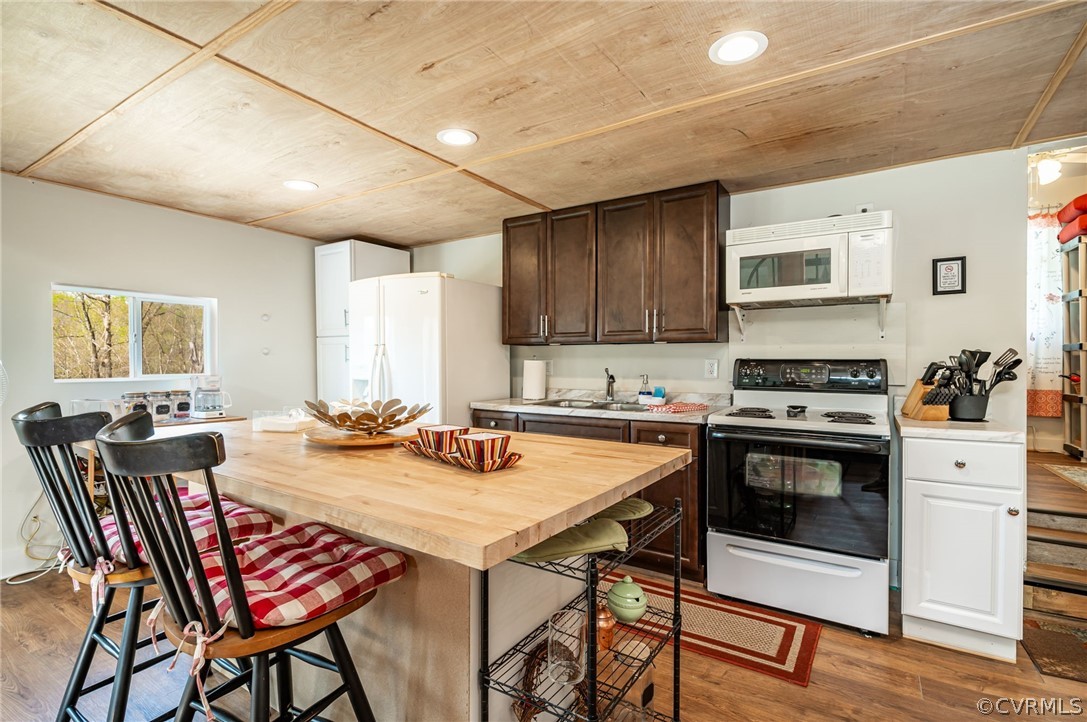 Kitchen featuring a breakfast bar area, white appliances, dark hardwood / wood-style flooring, sink, and dark brown cabinets