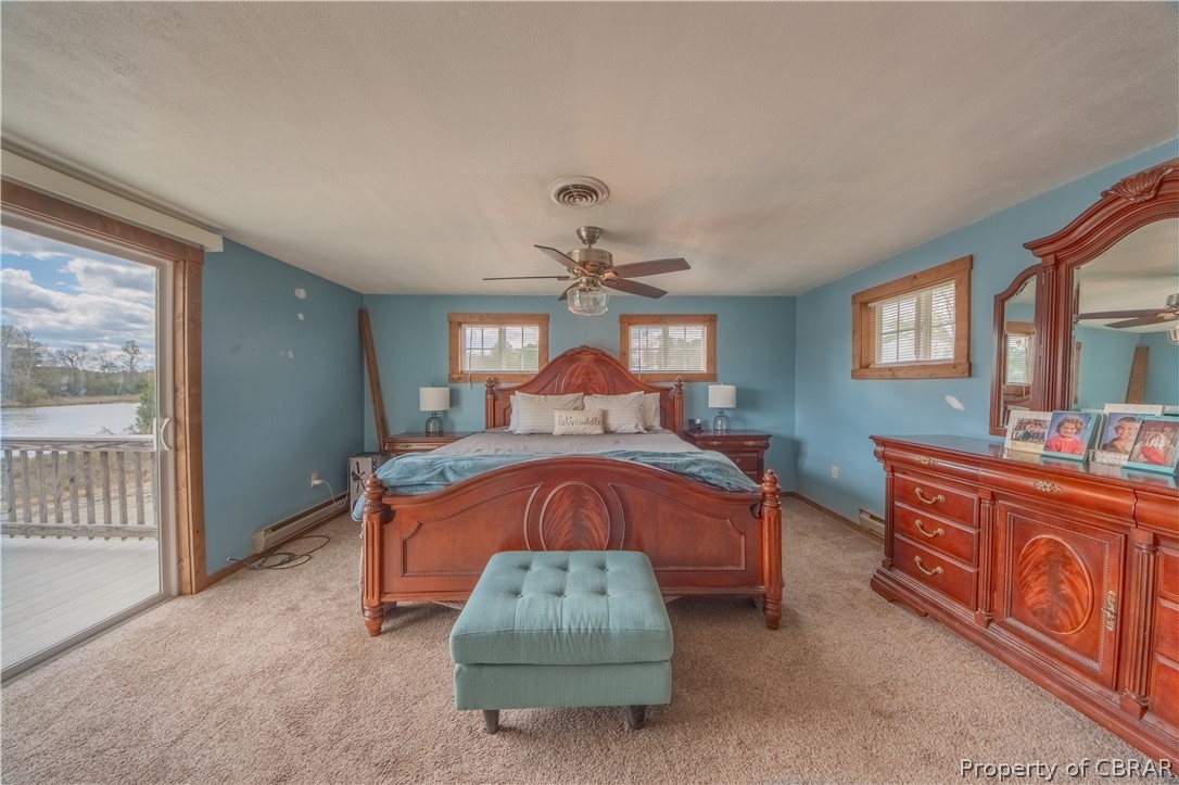 Carpeted bedroom with multiple windows, ceiling fan, access to exterior, and a baseboard heating unit