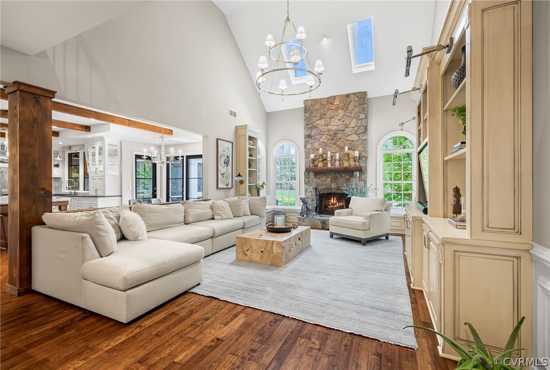 Living room with a stone fireplace, an inviting chandelier, dark wood-type flooring, and high vaulted ceiling