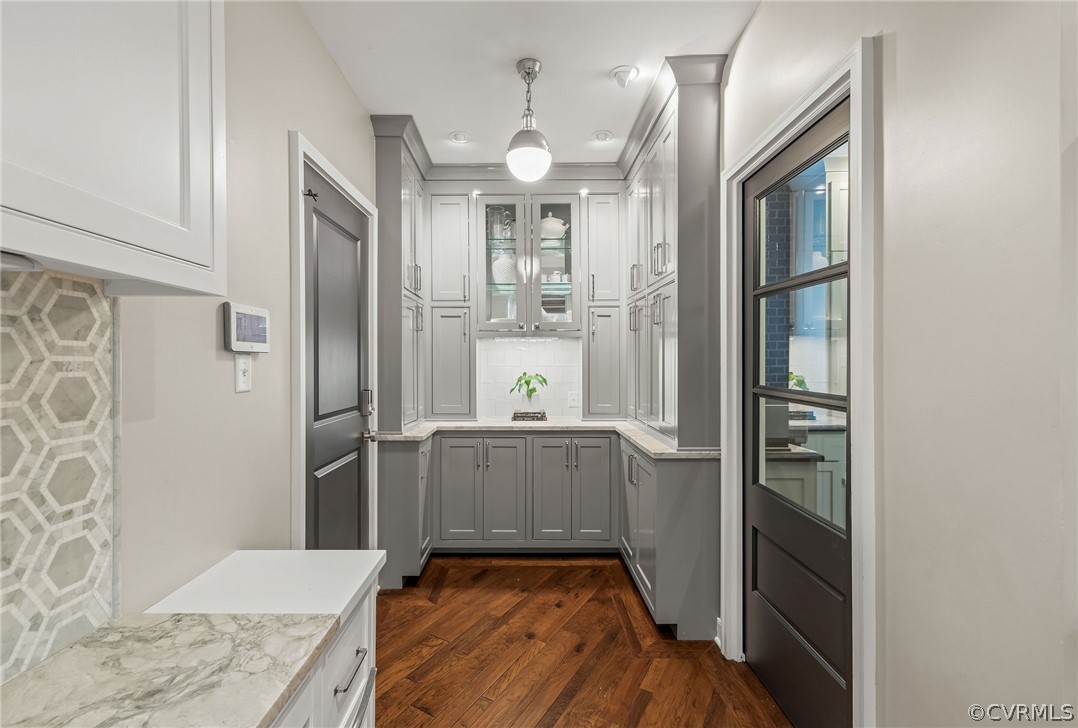 Kitchen with decorative light fixtures, light stone countertops, gray cabinets, dark hardwood / wood-style flooring, and tasteful backsplash