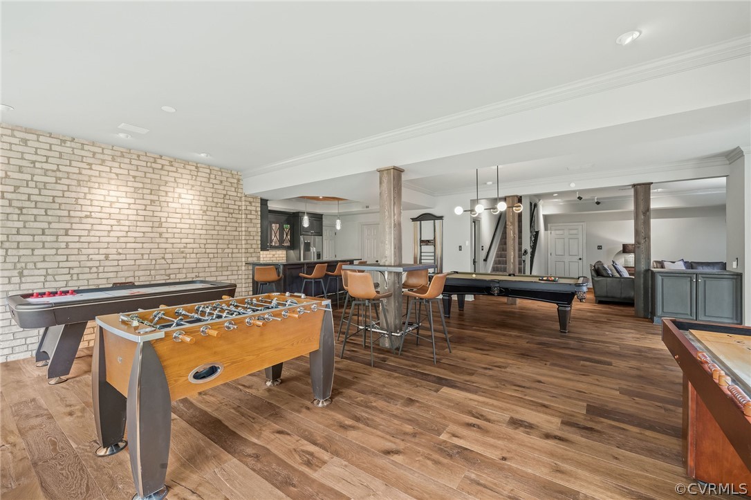 Rec room featuring billiards, indoor bar, brick wall, crown molding, and dark hardwood / wood-style floors