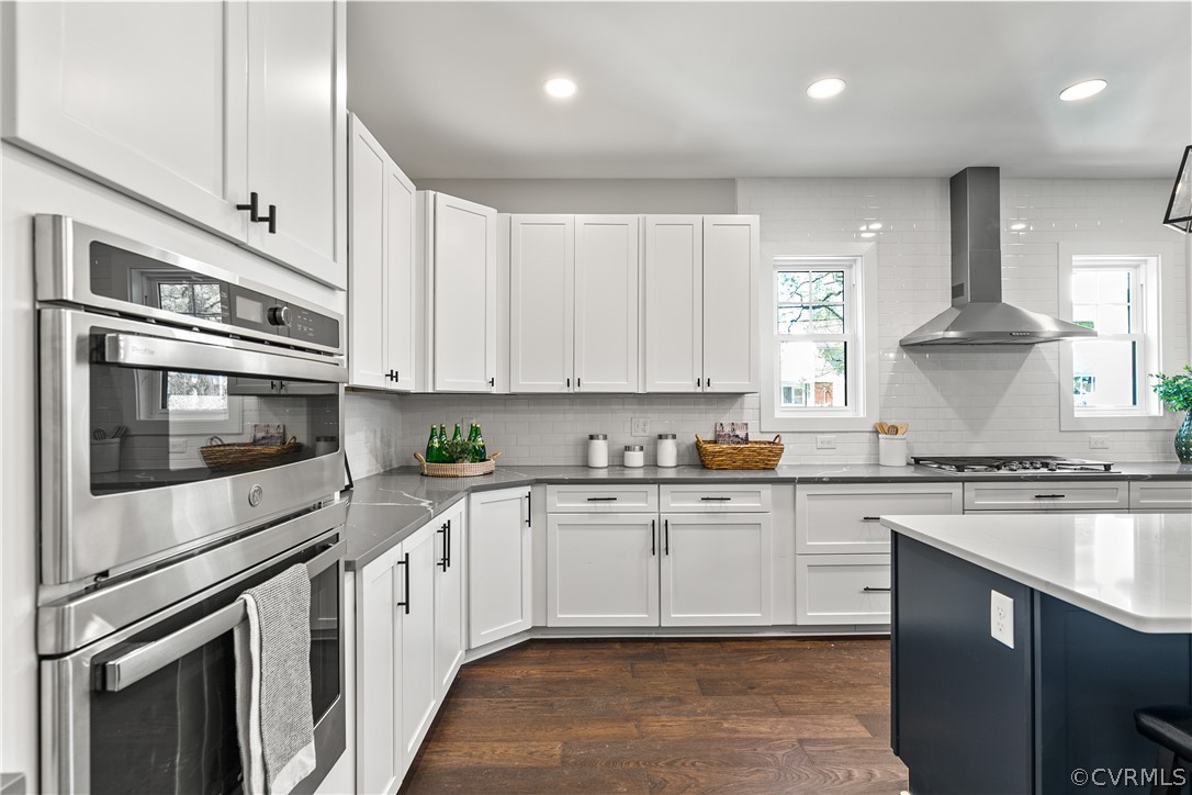 Kitchen featuring appliances with stainless steel finishes, backsplash, dark hardwood / wood-style floors, wall chimney exhaust hood, and white cabinets