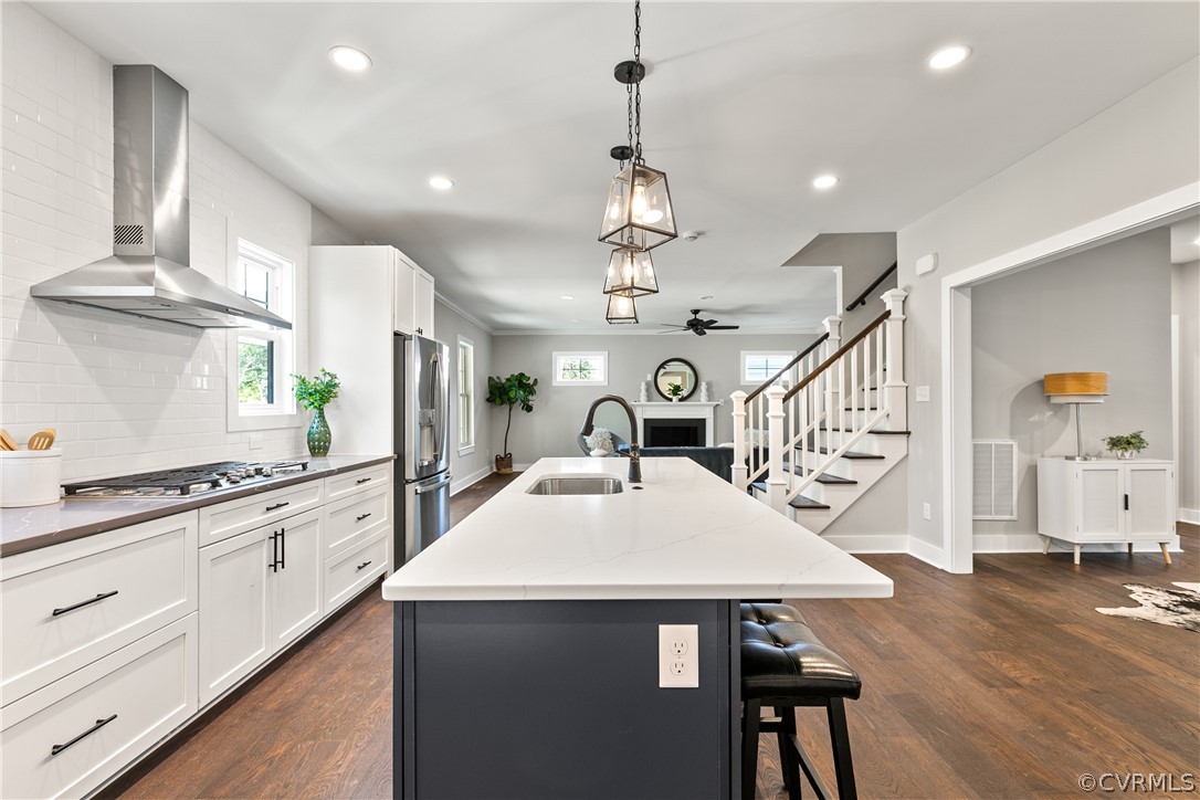 Kitchen featuring stainless steel appliances, dark hardwood / wood-style floors, tasteful backsplash, wall chimney range hood, and sink