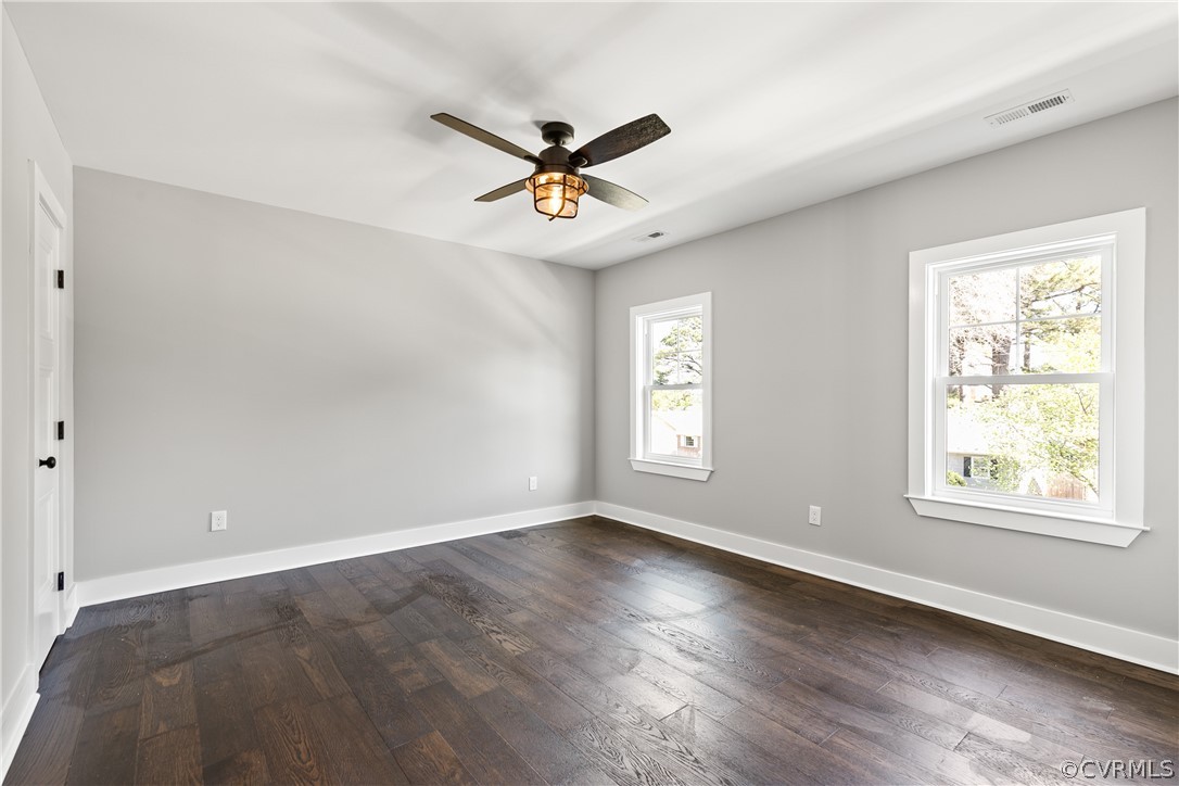 Empty room featuring a healthy amount of sunlight, ceiling fan, and dark wood-type flooring