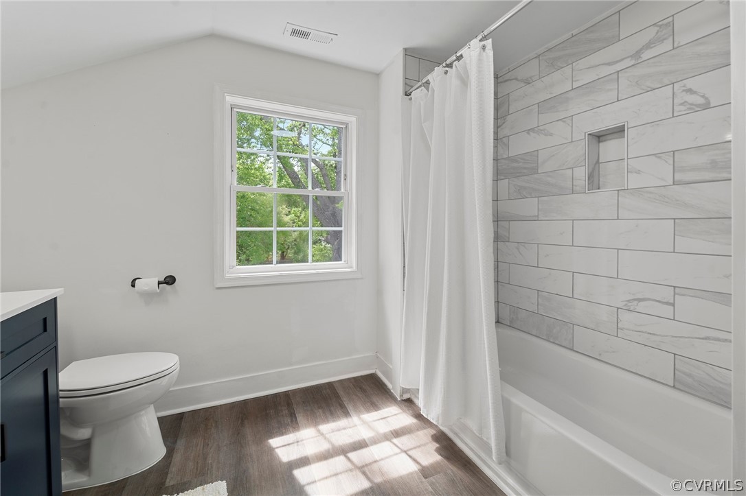 Full bathroom featuring shower / bath combination with curtain, vanity, hardwood / wood-style floors, vaulted ceiling, and toilet