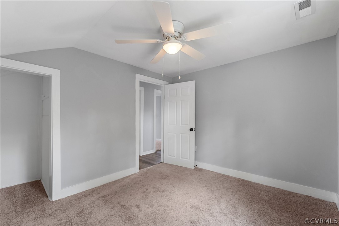Spare room featuring lofted ceiling, dark carpet, and ceiling fan