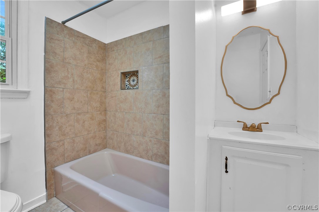 Full bathroom featuring tiled shower / bath combo, toilet, tile flooring, and vanity