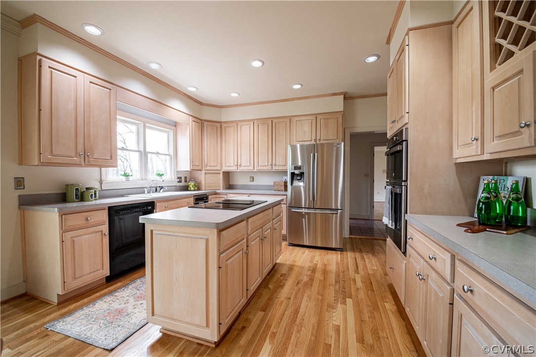 Kitchen featuring light brown cabinetry, light hardwood / wood-style flooring, a kitchen island, and black appliances