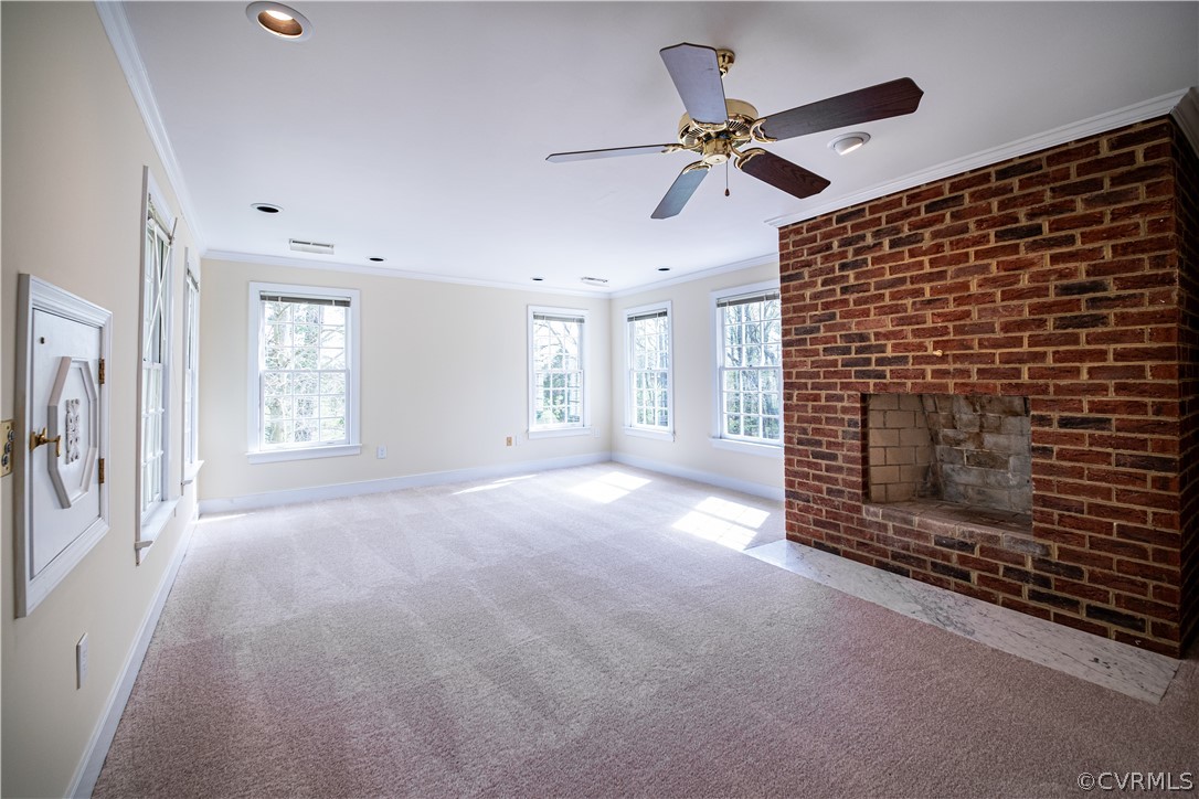 Primary bedroom featuring ornamental molding, ceiling fan, a brick fireplace, and light carpet