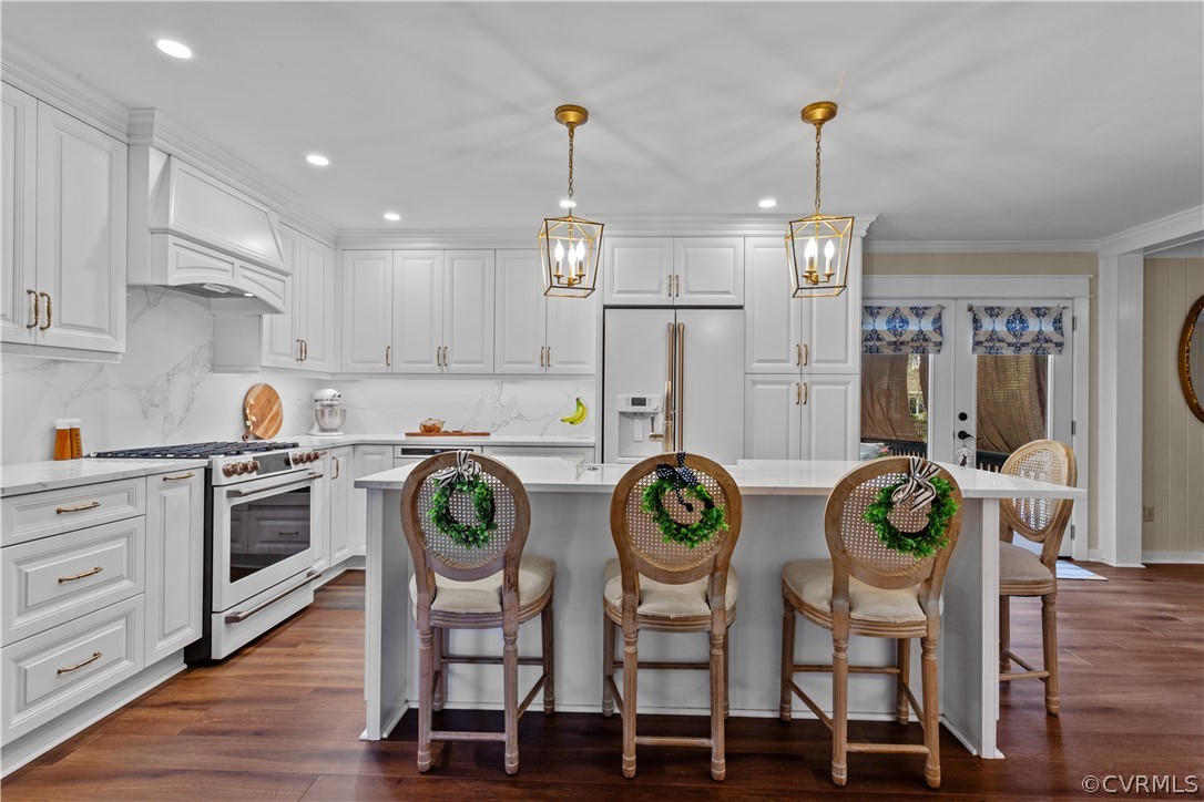 Kitchen with pendant lighting, white cabinets, premium appliances, dark wood-type flooring, and custom range hood