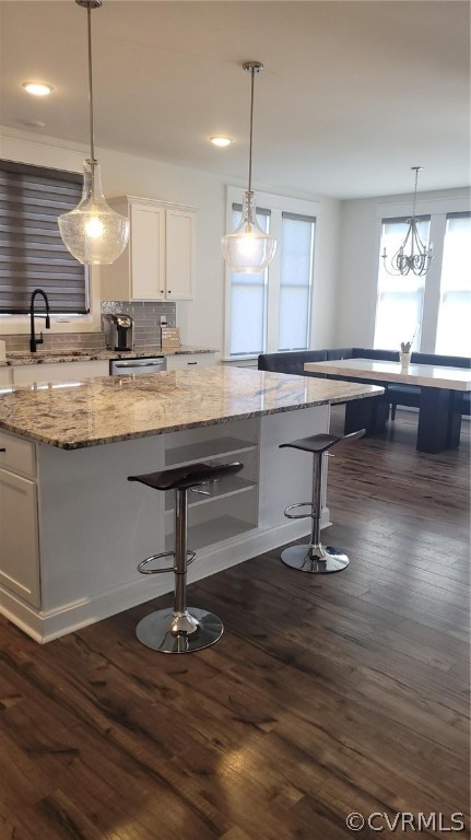 Kitchen with white cabinets, dark hardwood / wood-style flooring, light stone counters, and backsplash