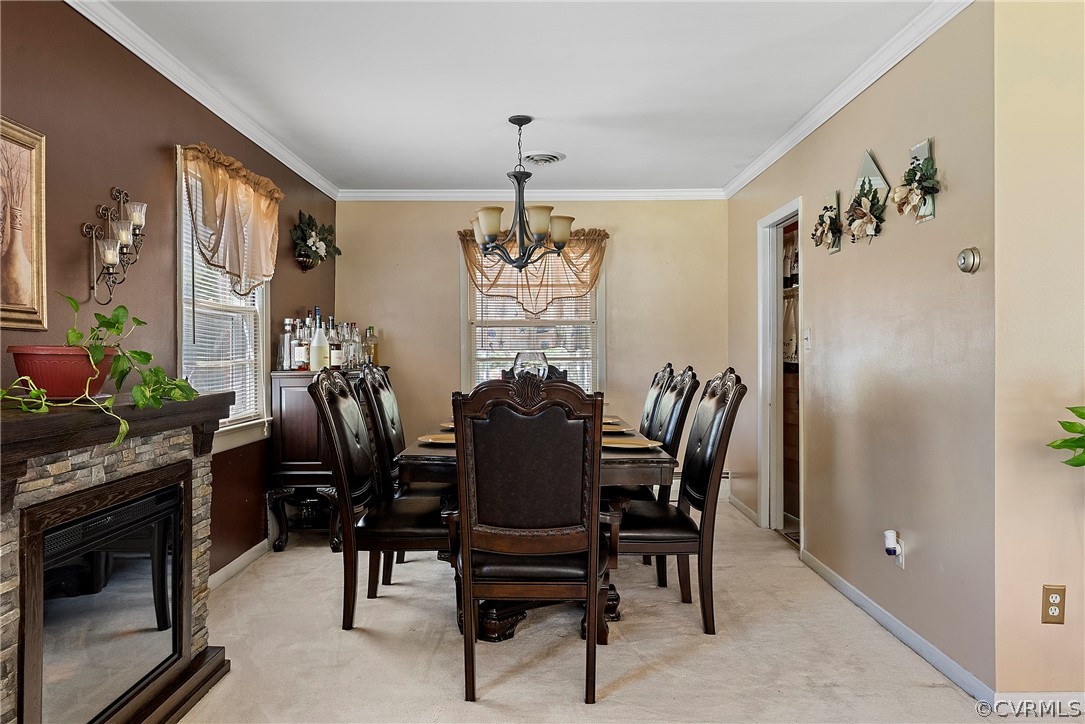 Carpeted dining space featuring a stone fireplace, crown molding, and a notable chandelier