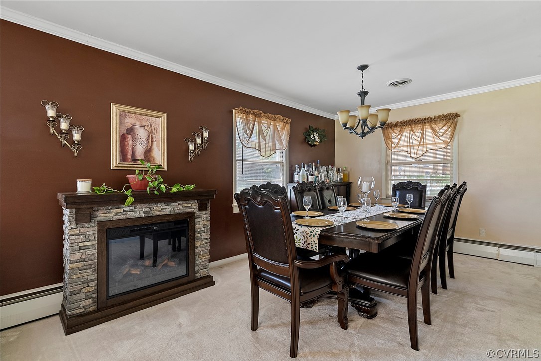 Dining space featuring light colored carpet, a baseboard radiator, a stone fireplace, and crown molding