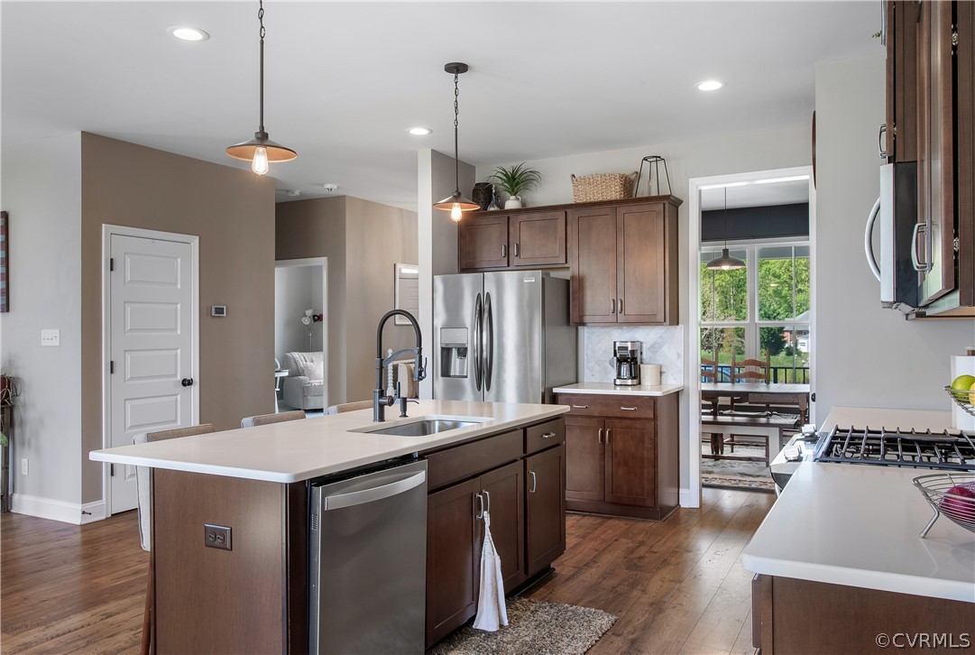 Kitchen with hanging light fixtures, a kitchen island with sink, stainless steel appliances, and dark wood-type flooring