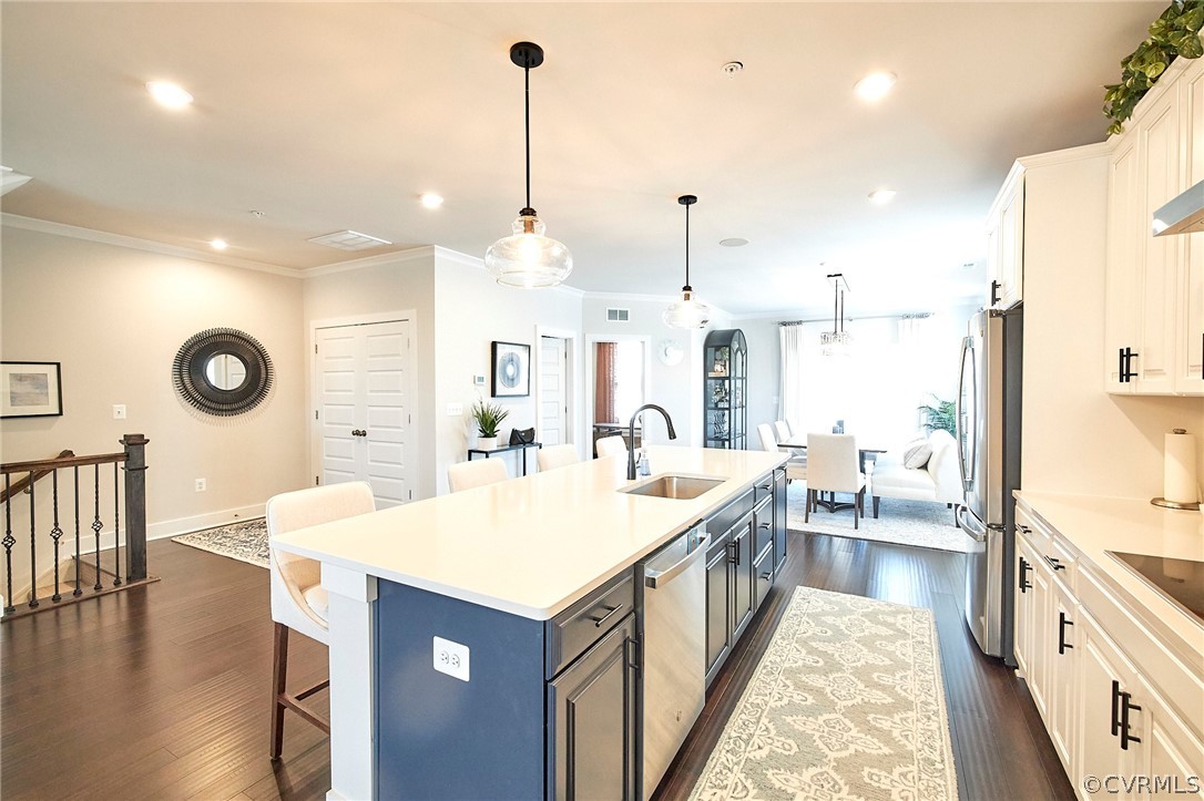 Kitchen with decorative light fixtures, a center island with sink, dark wood-type flooring, white cabinetry, and sink
