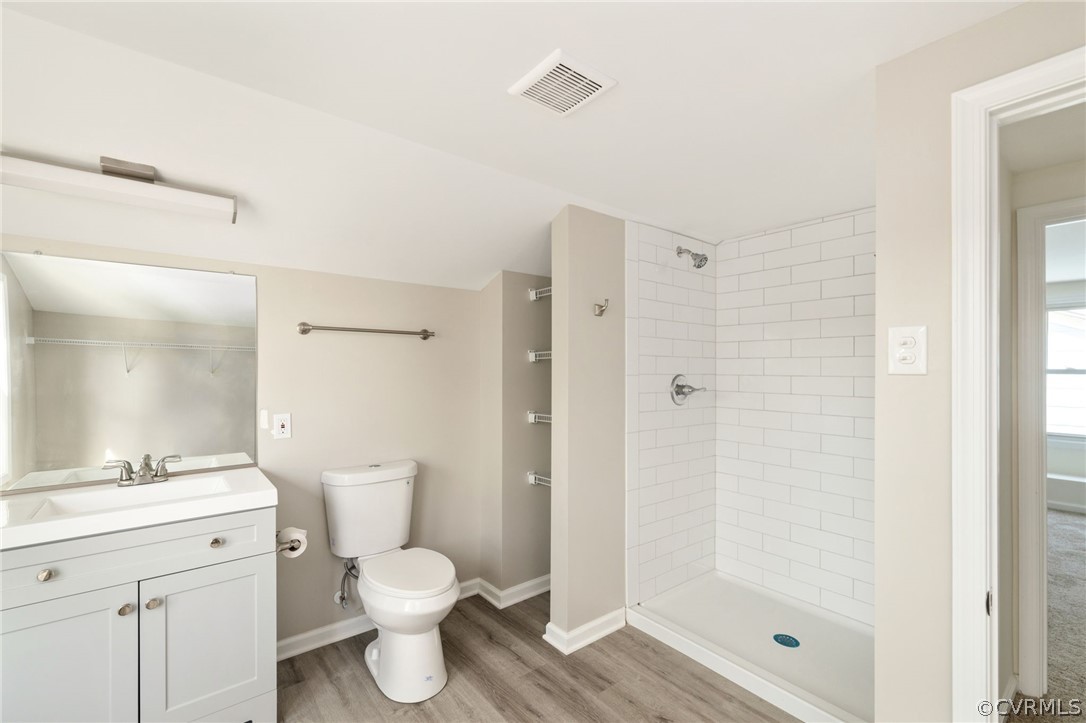 Bathroom with wood-type flooring, tiled shower, vanity with extensive cabinet space, and toilet