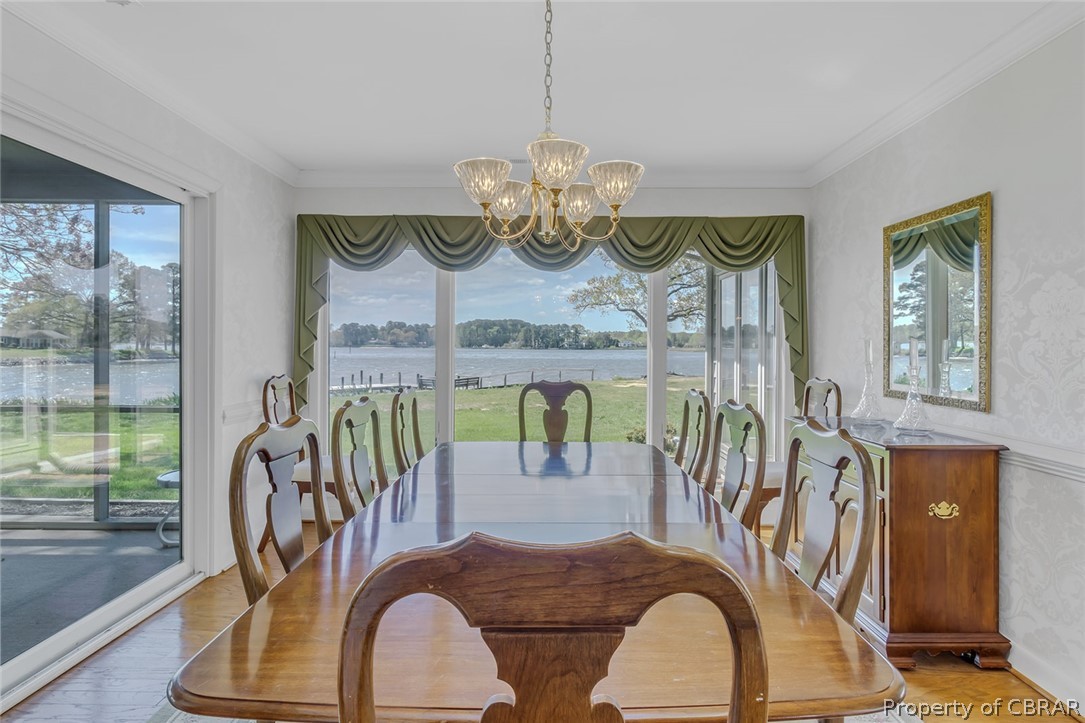 Dining area featuring a water view, light hardwood / wood-style floors, an inviting chandelier, and ornamental molding