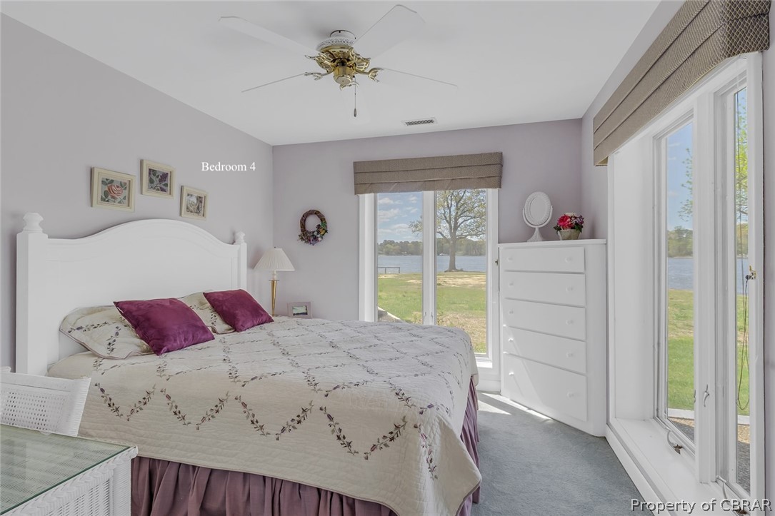 Carpeted bedroom with a water view, ceiling fan, and access to exterior