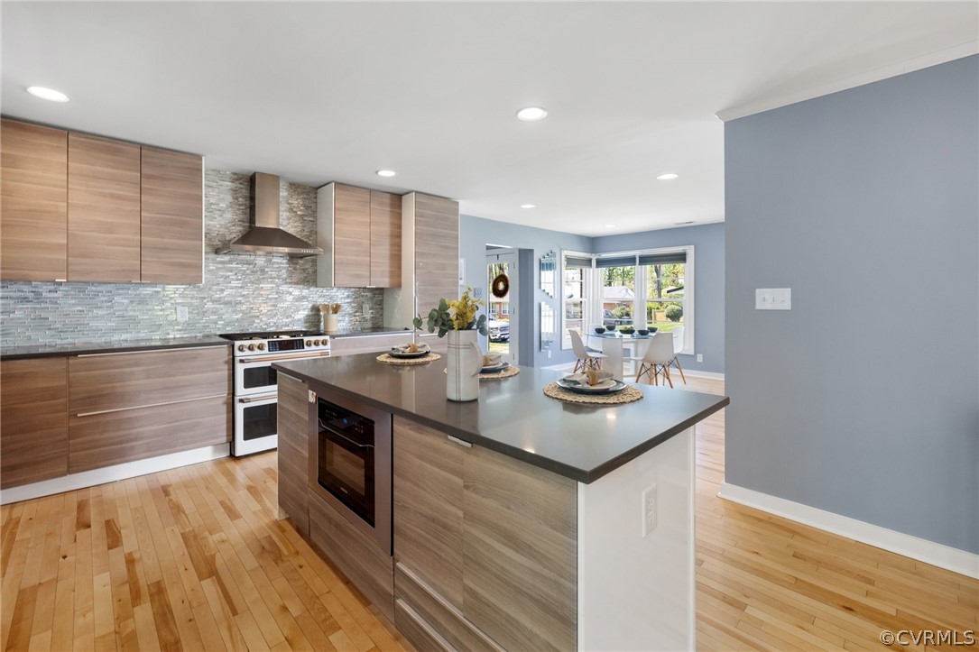 Kitchen featuring a center island, range with two ovens, wall chimney range hood, tasteful backsplash, and light hardwood / wood-style floors