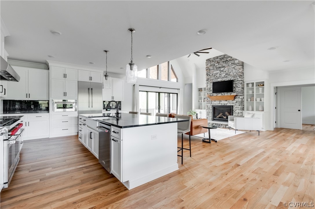 Kitchen featuring light hardwood / wood-style floors, high end appliances, a kitchen island with sink, white cabinetry, and a fireplace