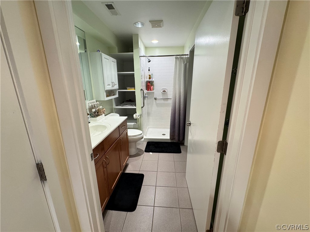 Bathroom featuring a shower with shower curtain, toilet, vanity with extensive cabinet space, and tile flooring