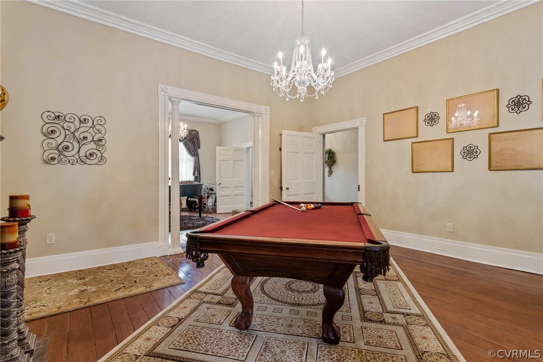 Rec room featuring dark hardwood / wood-style floors, pool table, crown molding, and an inviting chandelier
