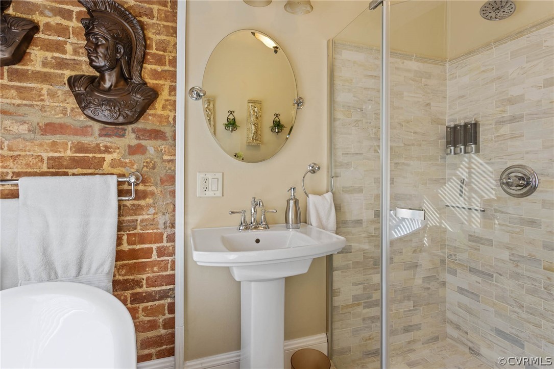Bathroom featuring brick wall and a shower with shower door