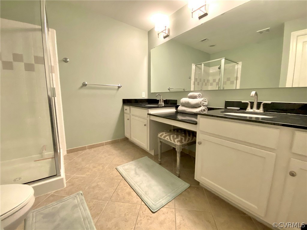 Bathroom featuring dual bowl vanity, an enclosed shower, toilet, and tile floors