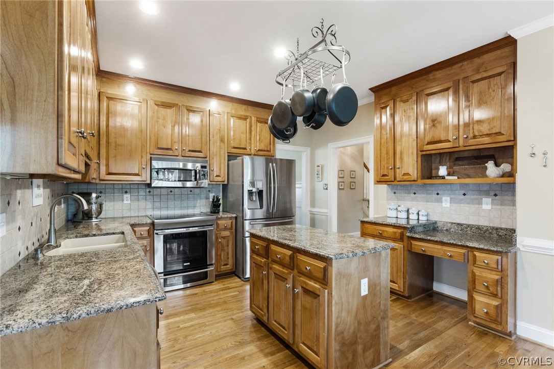 Kitchen featuring sink, light hardwood / wood-style floors, tasteful backsplash, stainless steel appliances, and light stone countertops