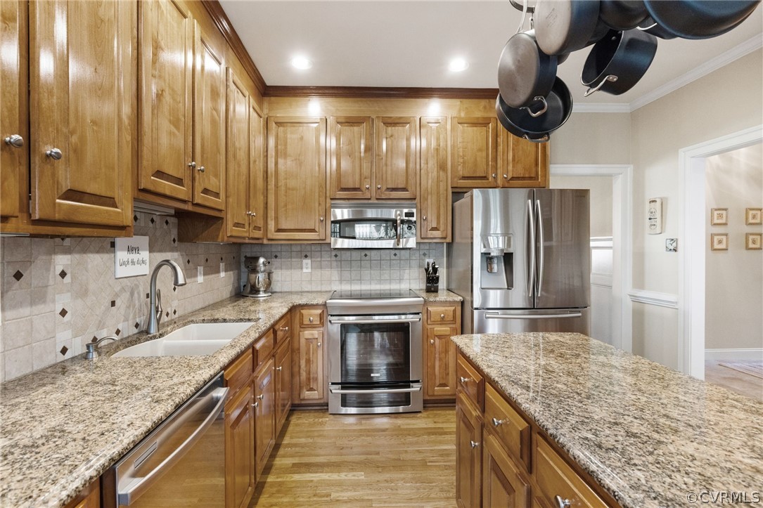 Kitchen with light hardwood / wood-style flooring, stainless steel appliances, tasteful backsplash, light stone counters, and sink