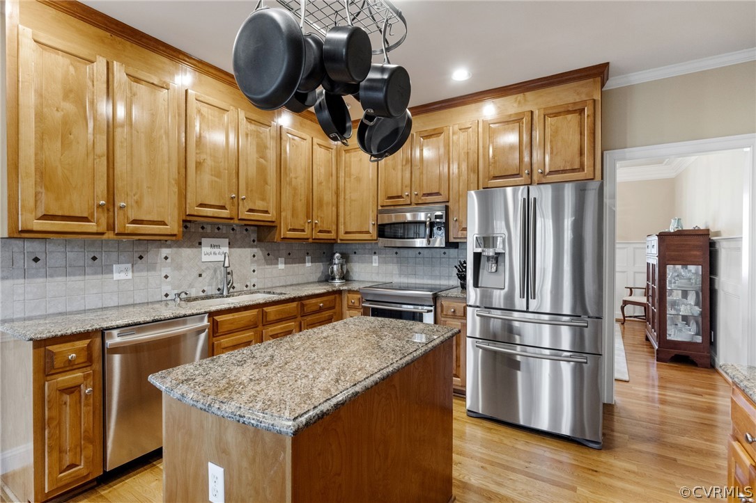 Kitchen with light stone countertops, light hardwood / wood-style flooring, backsplash, appliances with stainless steel finishes, and a kitchen island