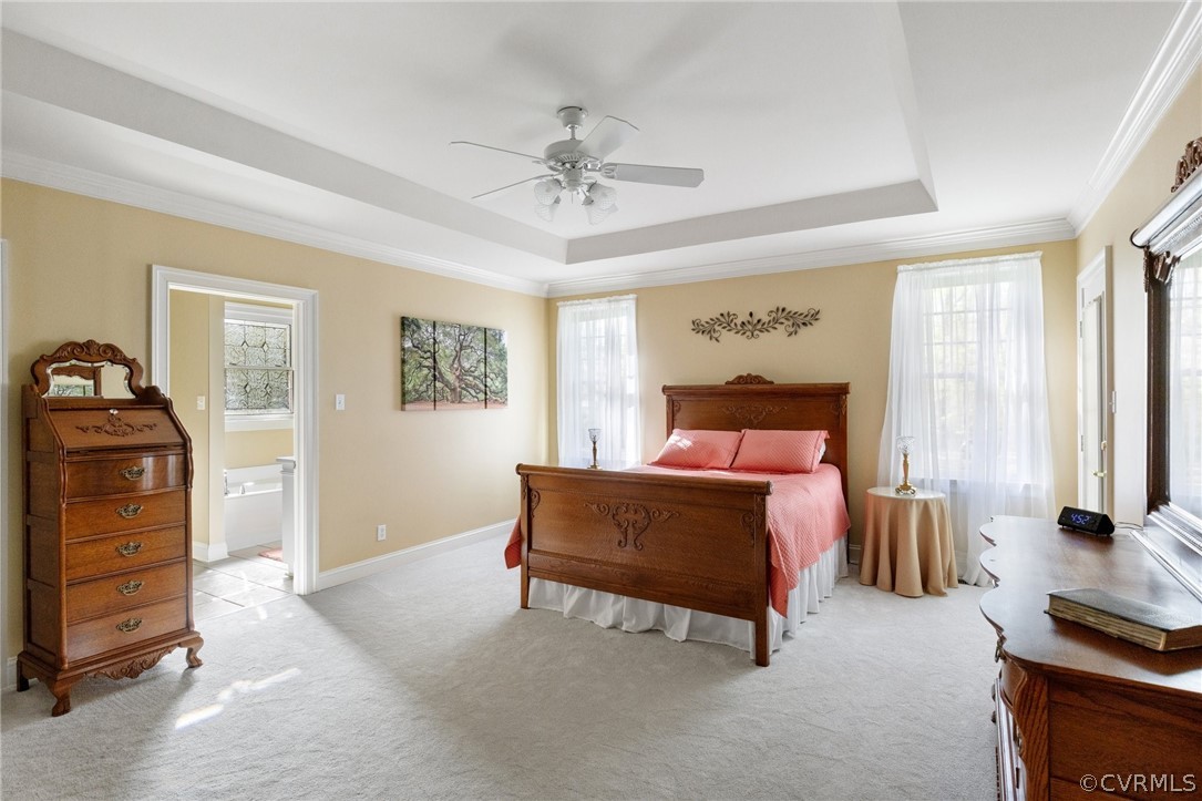 Bedroom with light colored carpet, ceiling fan, crown molding, a tray ceiling, and connected bathroom