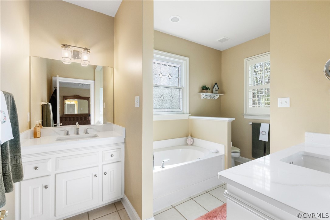 Bathroom with a tub, a healthy amount of sunlight, toilet, and large vanity