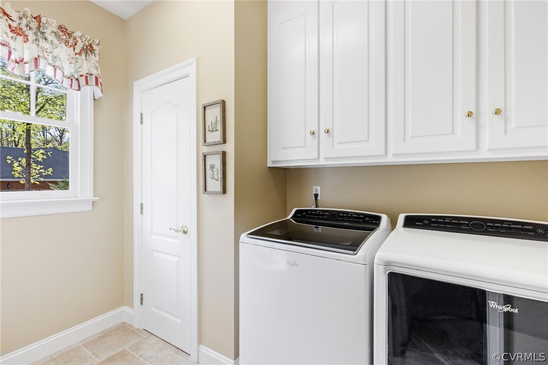 Clothes washing area with cabinets, light tile floors, and washer and clothes dryer