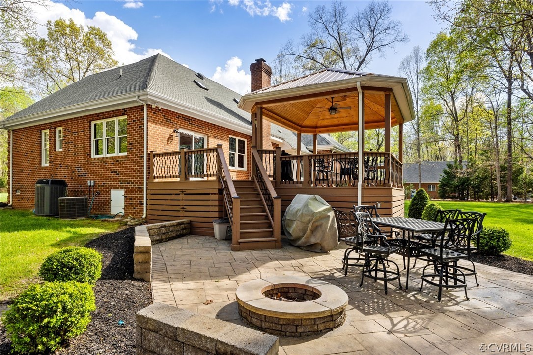 Back of property featuring a deck, a patio, central air condition unit, an outdoor fire pit, and a lawn