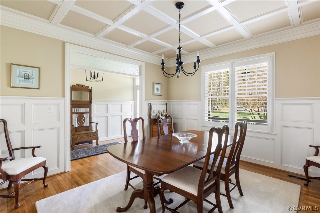 Dining area featuring light wood-type flooring, coffered ceiling, and a chandelier