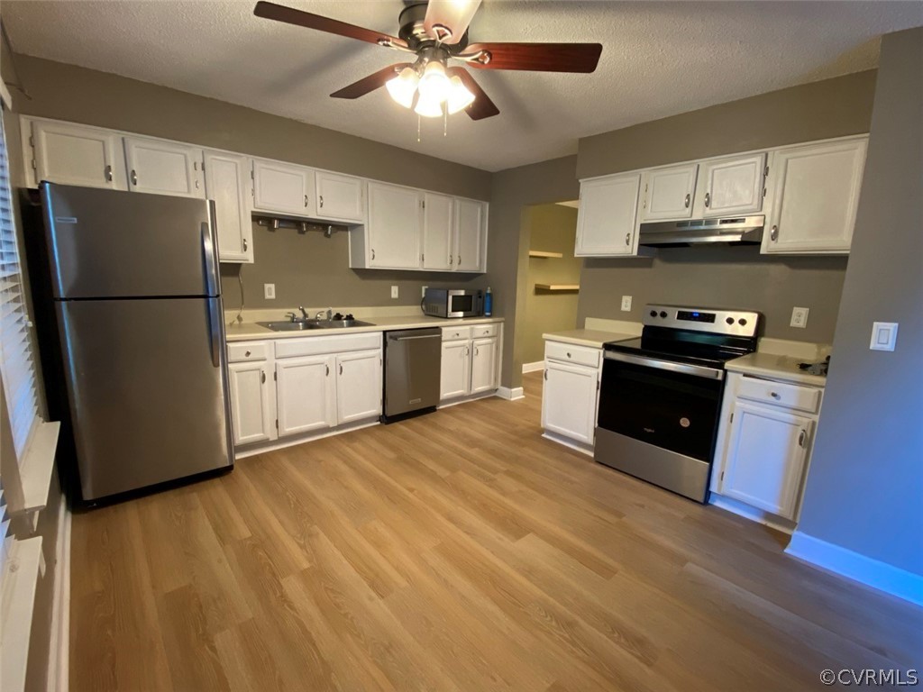 Kitchen with white cabinets, ceiling fan, light wood-type flooring, and stainless steel appliances