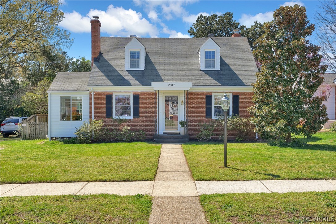Brick Cape Cod style home with a front lawn