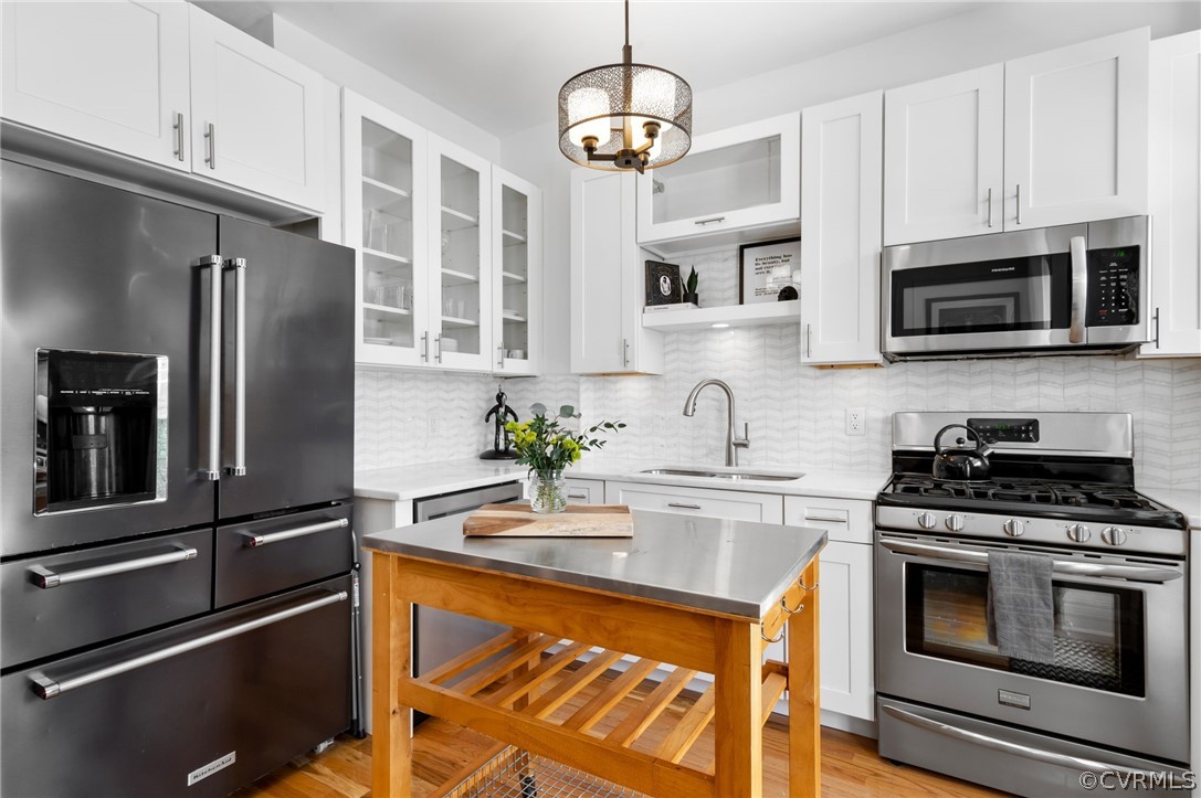 Kitchen featuring backsplash, sink, stainless steel appliances, and white cabinetry