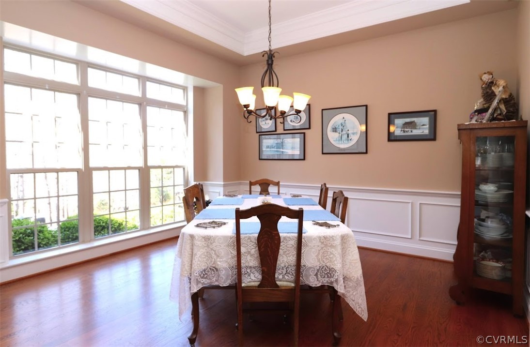 Dining room with ornamental molding, dark wood flooring, a notable chandelier, and a tray ceiling