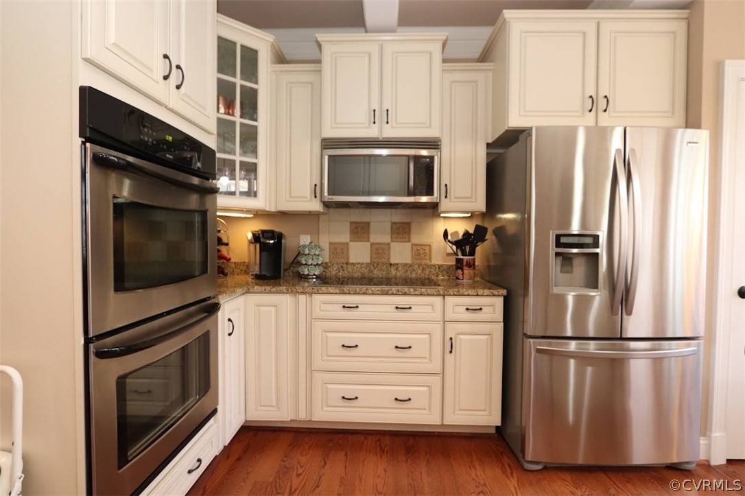 Kitchen featuring white cabinets, dark hardwood / wood-style flooring, stainless steel appliances, tasteful backsplash, and dark stone counters