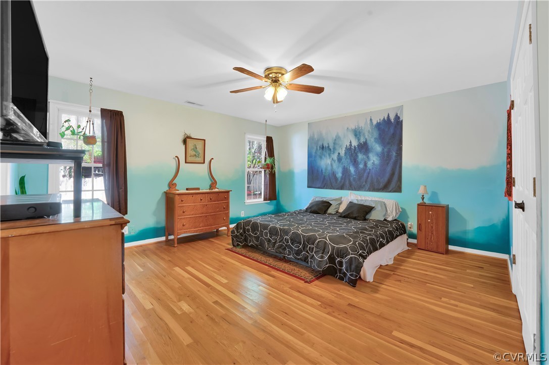 Bedroom with light hardwood / wood-style floors, ceiling fan, and multiple windows