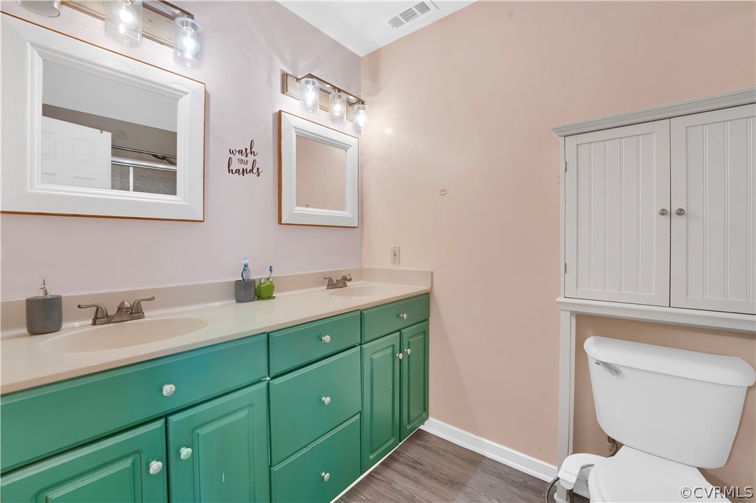 Bathroom with double sink, wood-type flooring, oversized vanity, and toilet