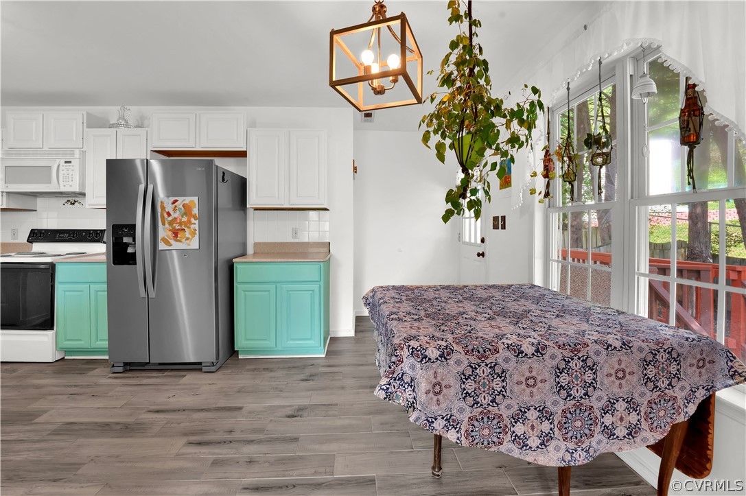Kitchen with decorative light fixtures, white appliances, light hardwood / wood-style floors, tasteful backsplash, and white cabinets