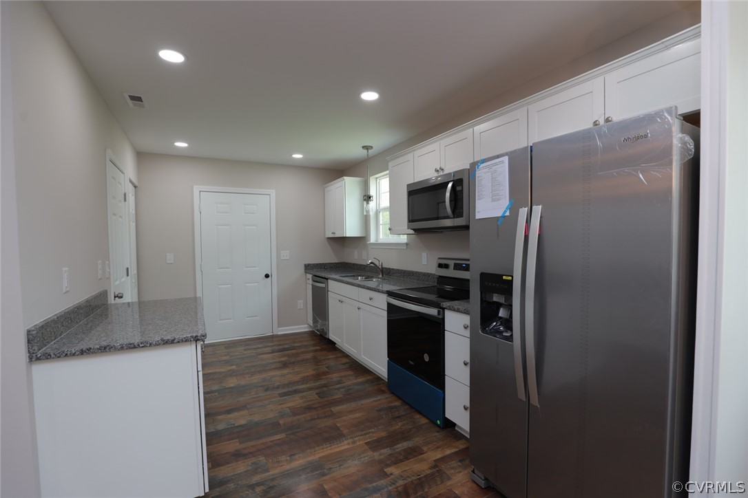 Kitchen with dark hardwood / wood-style flooring, appliances with stainless steel finishes, white cabinetry, and sink
