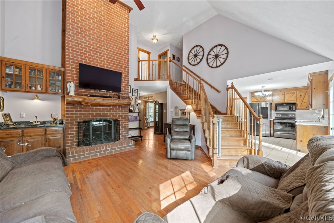 Living room featuring brick wall, a brick fireplace, high vaulted ceiling, and light wood-type flooring