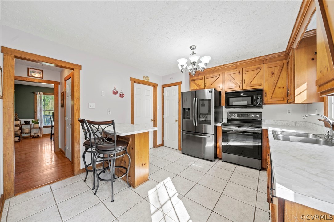 Kitchen featuring stainless steel refrigerator with ice dispenser, sink, light tile floors, range with electric stovetop, and a breakfast bar area