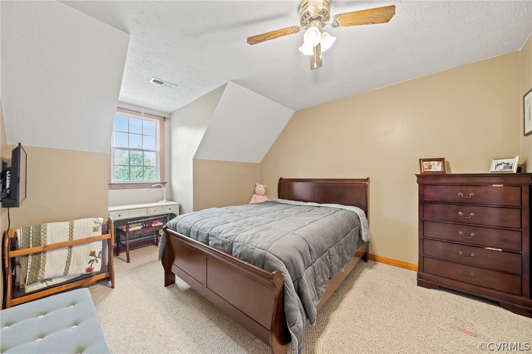 Carpeted bedroom with vaulted ceiling, ceiling fan, and a textured ceiling