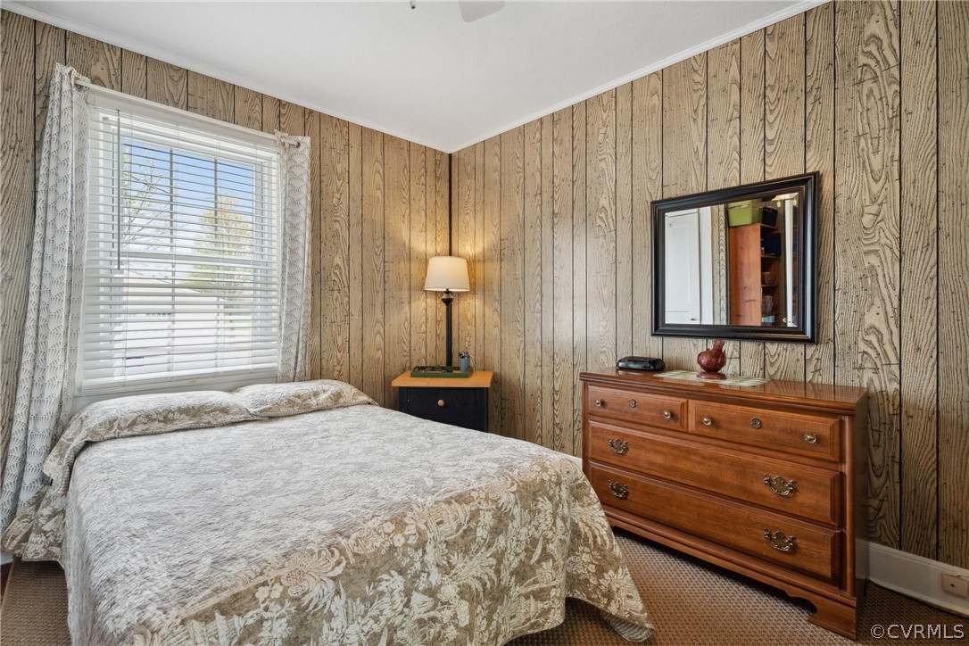 Carpeted bedroom featuring wood walls, crown molding, and ceiling fan
