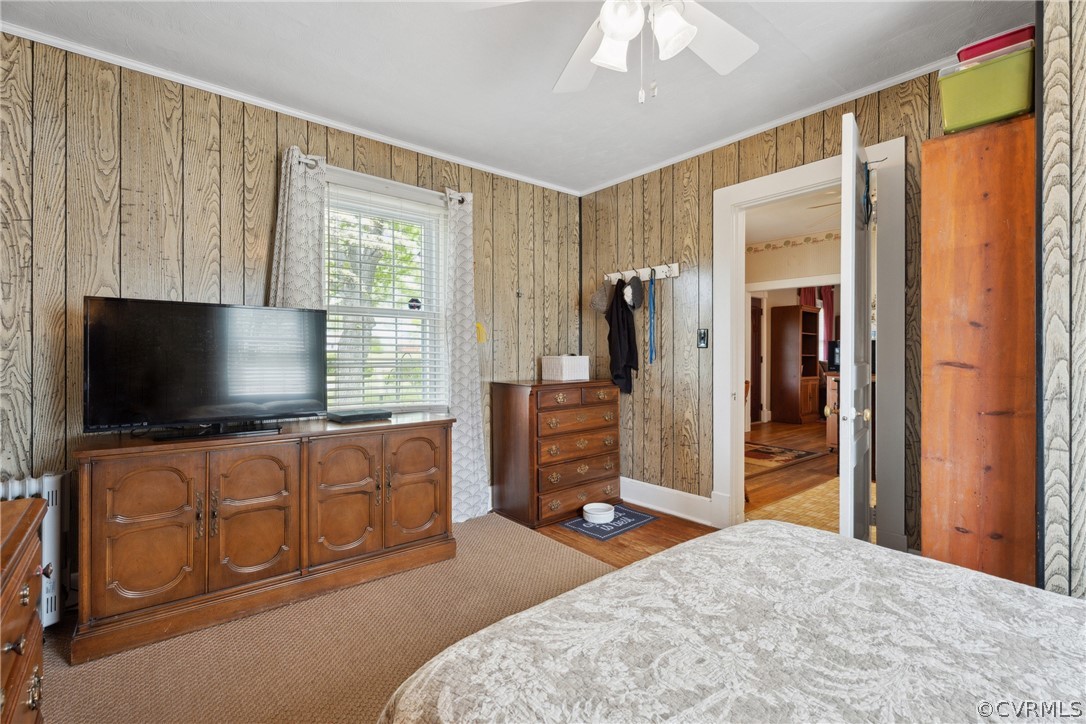 Bedroom with wood walls, dark wood-type flooring, and ceiling fan